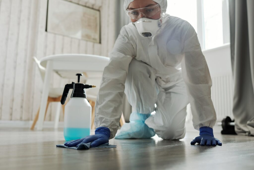 a woman in white coveralls wiping a floor while wearing gloves